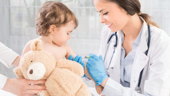 Junge Frau Kinderarztin führt eine Impfung eines kleinen Mädchens durch. Das Mädchen hält ein Maskottchen.